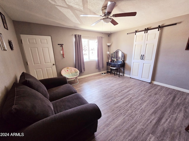 living room featuring ceiling fan, hardwood / wood-style floors, a barn door, and a textured ceiling