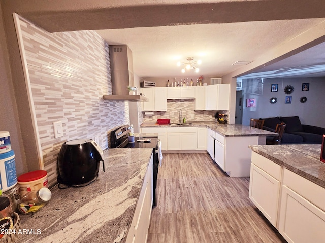 kitchen with wall chimney exhaust hood, stainless steel range with electric cooktop, tasteful backsplash, white cabinets, and sink