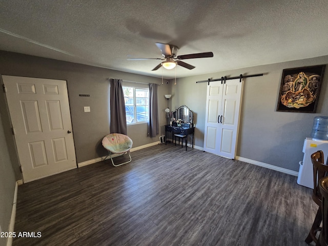 miscellaneous room with ceiling fan, dark wood-type flooring, a barn door, and a textured ceiling