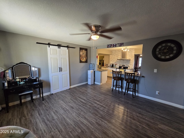 living room featuring a textured ceiling, dark hardwood / wood-style flooring, a barn door, and ceiling fan with notable chandelier