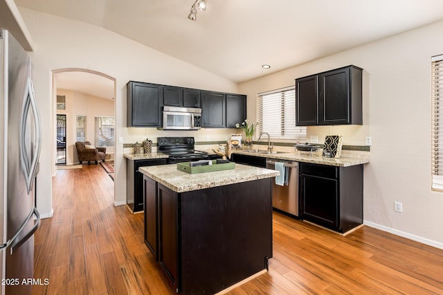 kitchen with stainless steel appliances, a center island, light stone counters, light hardwood / wood-style flooring, and lofted ceiling