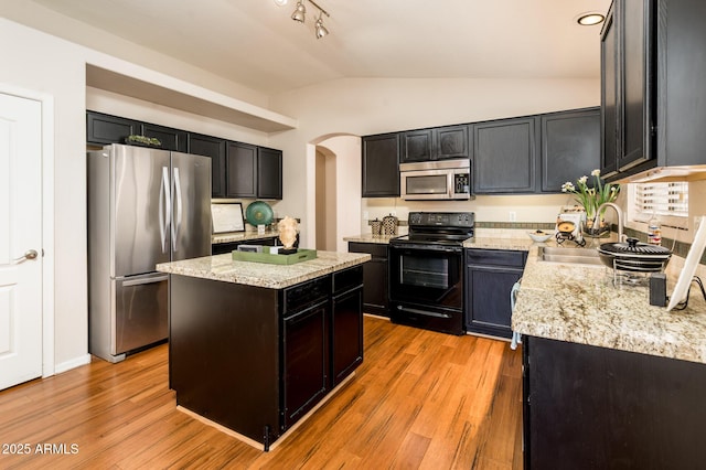 kitchen with stainless steel appliances, sink, vaulted ceiling, light hardwood / wood-style floors, and a kitchen island