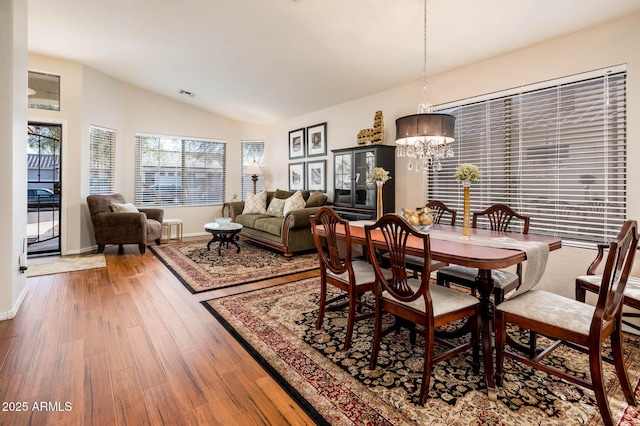 dining space featuring hardwood / wood-style flooring, an inviting chandelier, and vaulted ceiling