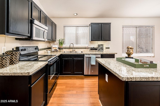 kitchen featuring light stone counters, appliances with stainless steel finishes, light hardwood / wood-style floors, and sink