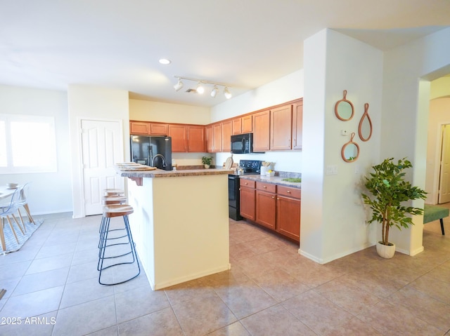 35721 N Zachary Rd, Queen Creek, AZ 85144 - kitchen featuring a kitchen island with sink, a kitchen bar, brown cabinets, light tile patterned floors, and black appliances