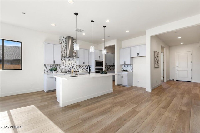 kitchen with appliances with stainless steel finishes, light wood-type flooring, backsplash, and wall chimney exhaust hood