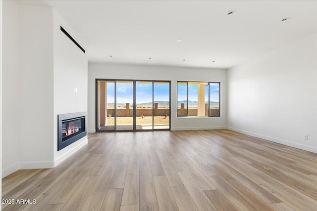 unfurnished living room with light wood finished floors, a glass covered fireplace, and baseboards