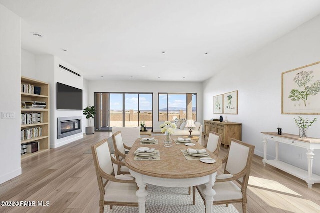 dining room featuring light wood-type flooring, a glass covered fireplace, and baseboards