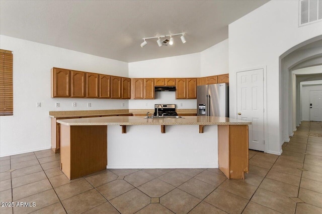 kitchen with high end refrigerator, visible vents, a center island with sink, light countertops, and under cabinet range hood