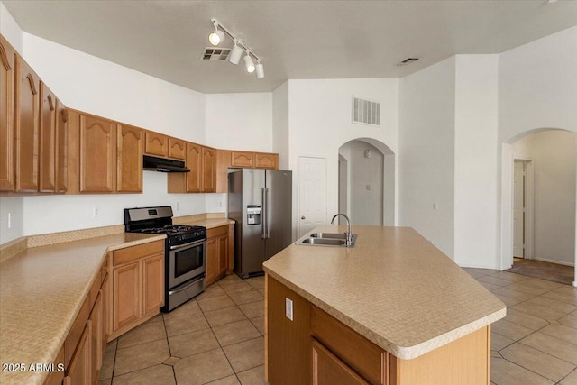 kitchen with arched walkways, a kitchen island with sink, stainless steel appliances, a sink, and light countertops