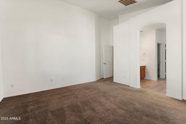 spare room featuring baseboards, visible vents, arched walkways, and light colored carpet