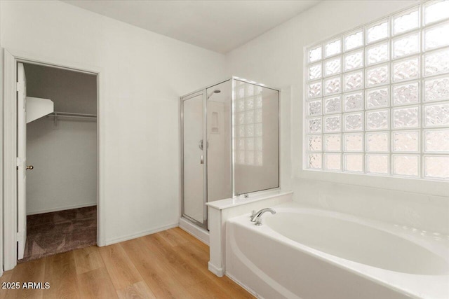 full bath featuring a garden tub, a shower stall, a walk in closet, and wood finished floors