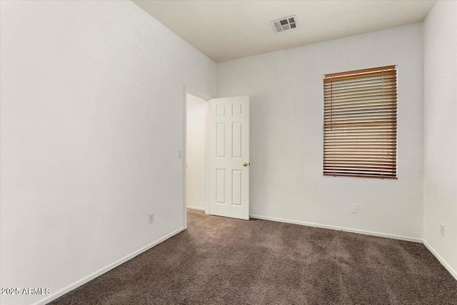 spare room featuring baseboards, visible vents, and dark colored carpet