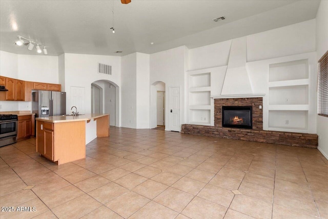 kitchen with built in shelves, light countertops, appliances with stainless steel finishes, open floor plan, and an island with sink