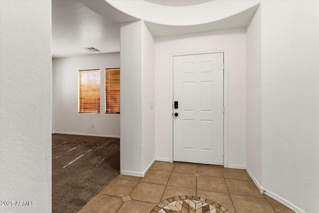 tiled entryway with baseboards, visible vents, and a textured wall