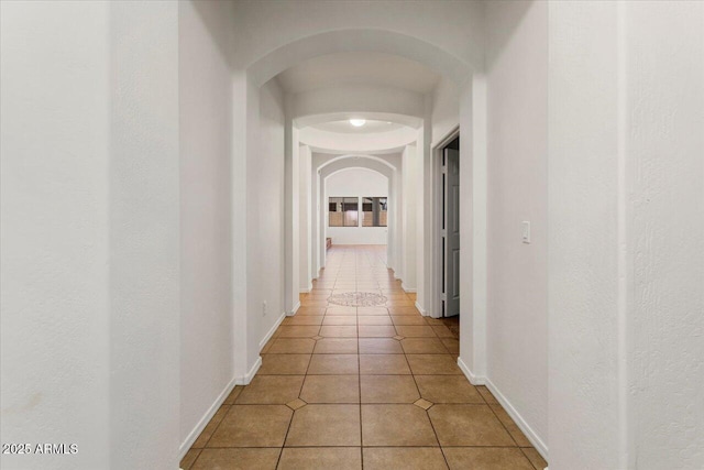 hallway with light tile patterned floors, baseboards, and arched walkways