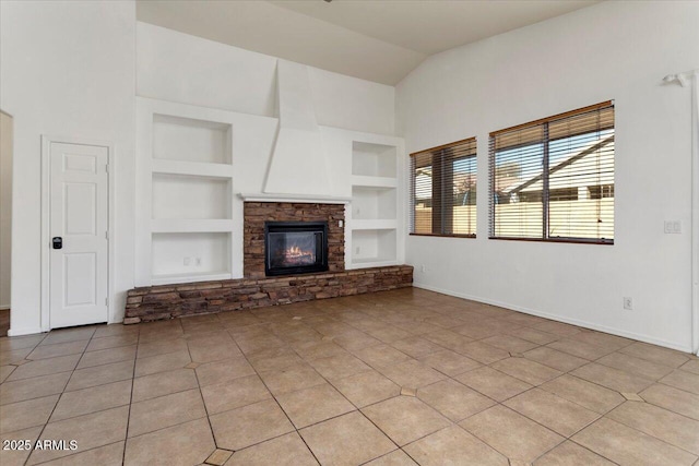 unfurnished living room with light tile patterned floors, baseboards, built in features, lofted ceiling, and a fireplace