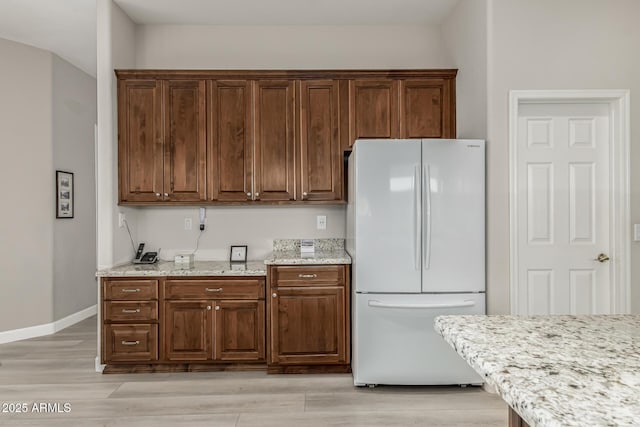 kitchen with light wood-type flooring, white refrigerator, and light stone counters