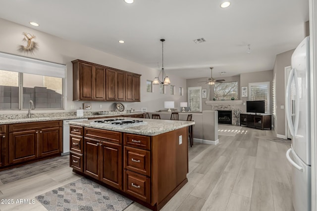 kitchen with decorative light fixtures, light hardwood / wood-style floors, a center island, sink, and white appliances