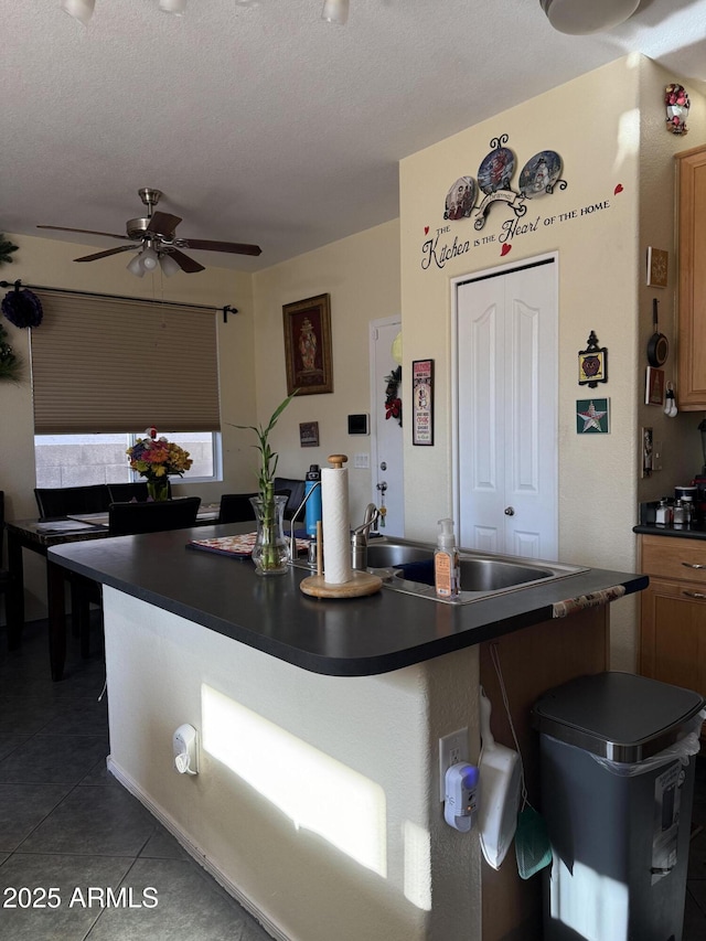 1448 E Mobile Ln, Phoenix, AZ 85040 - kitchen with dark countertops, a ceiling fan, a kitchen island with sink, a breakfast bar, and dark tile patterned flooring