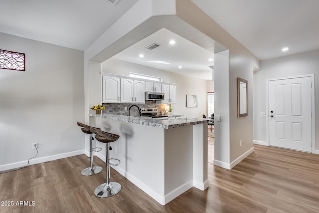 kitchen with kitchen peninsula, light hardwood / wood-style flooring, appliances with stainless steel finishes, a kitchen bar, and white cabinetry