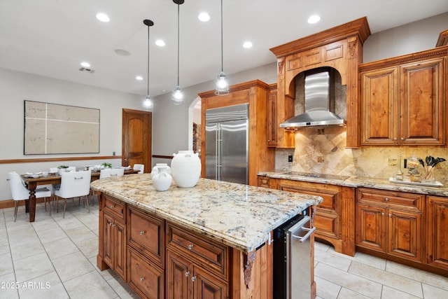 kitchen featuring hanging light fixtures, wall chimney exhaust hood, built in refrigerator, backsplash, and a center island