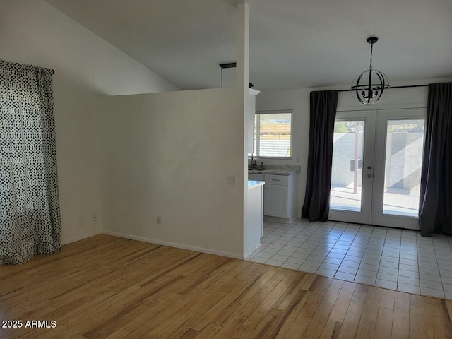 interior space with french doors, sink, a chandelier, vaulted ceiling, and light hardwood / wood-style floors