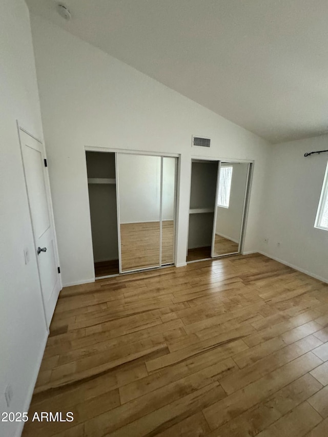 unfurnished bedroom with two closets, high vaulted ceiling, and light wood-type flooring