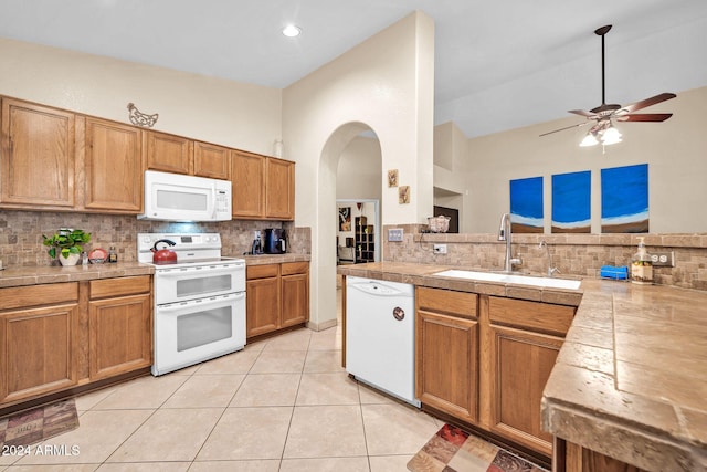 kitchen with a towering ceiling, decorative backsplash, sink, light tile patterned flooring, and white appliances