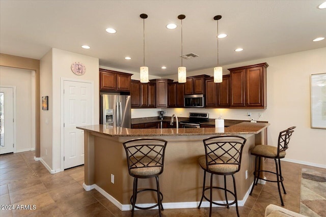 kitchen featuring a kitchen breakfast bar, hanging light fixtures, a kitchen island with sink, and appliances with stainless steel finishes