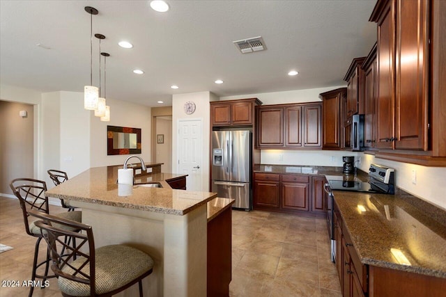 kitchen with a kitchen bar, stainless steel appliances, a kitchen island with sink, and dark stone countertops