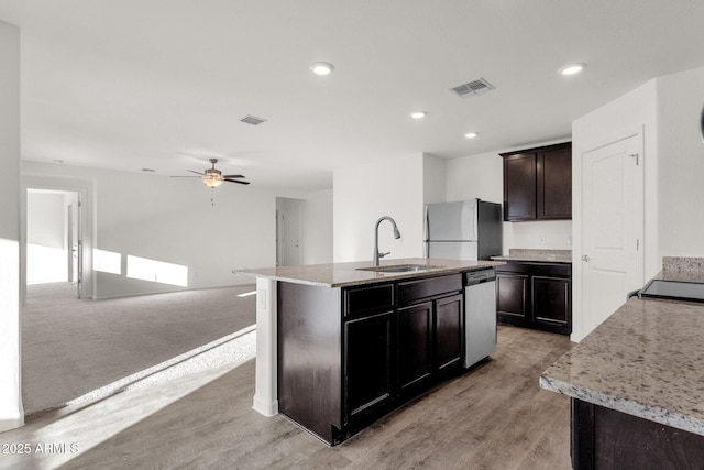 kitchen featuring a kitchen island with sink, light hardwood / wood-style floors, ceiling fan, sink, and fridge