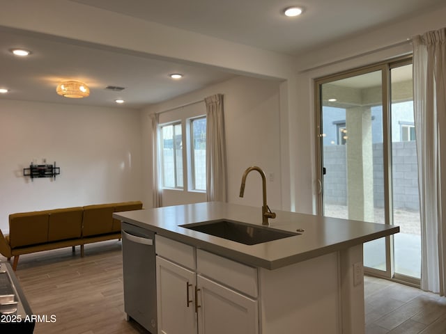 kitchen featuring dishwasher, an island with sink, sink, white cabinets, and light hardwood / wood-style flooring