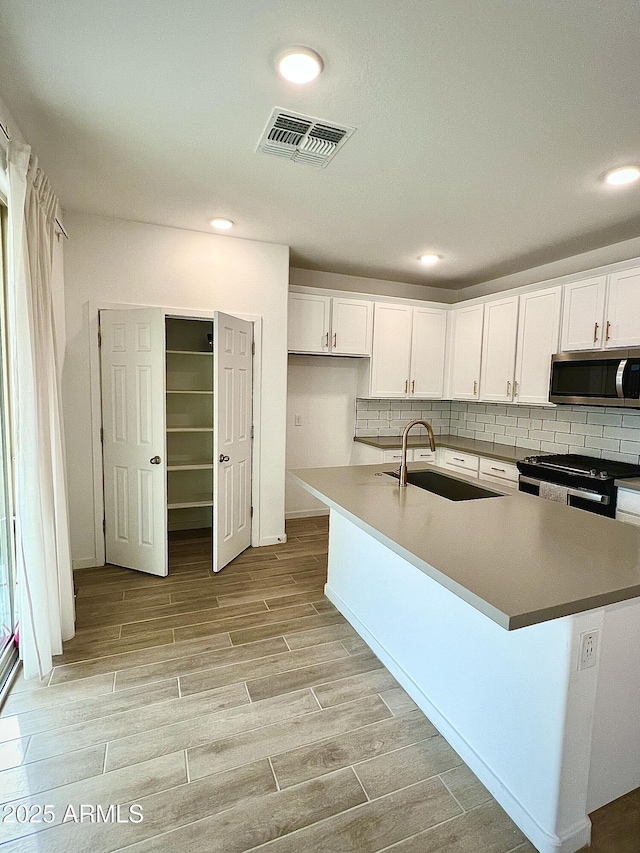 kitchen featuring sink, black range with gas stovetop, an island with sink, and white cabinets