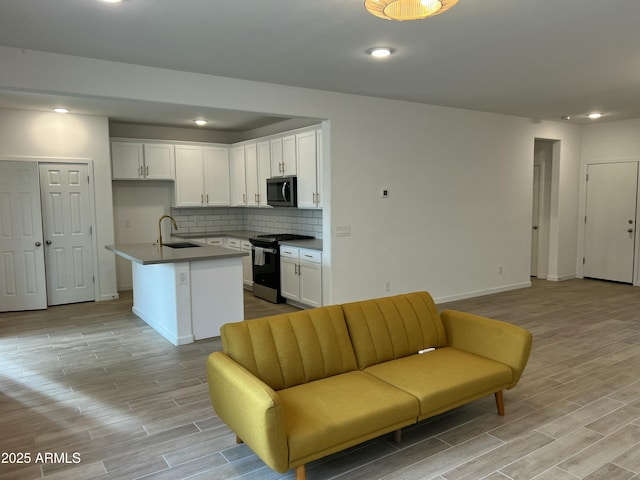 kitchen featuring sink, range with gas cooktop, a center island with sink, white cabinets, and backsplash