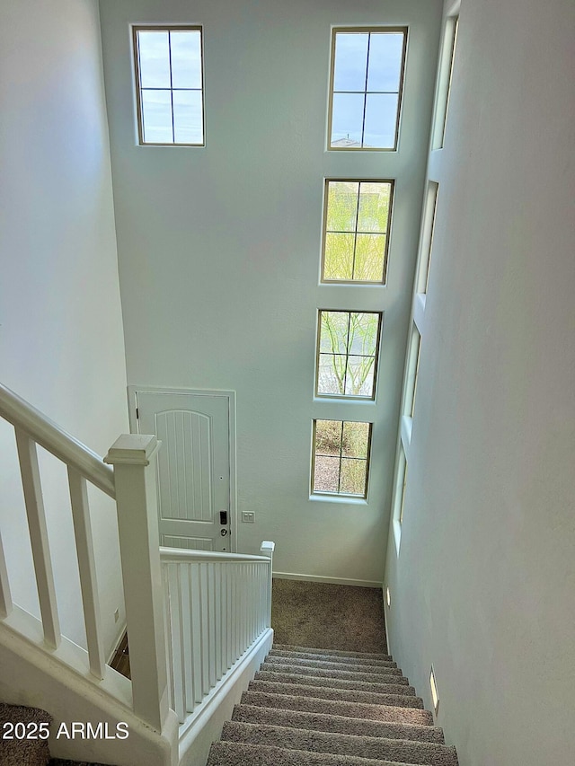 staircase featuring a towering ceiling, plenty of natural light, and carpet