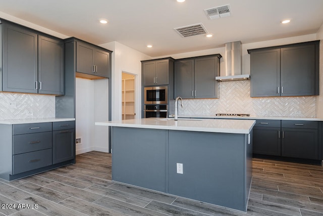 kitchen with sink, a kitchen island with sink, wall chimney range hood, and dark hardwood / wood-style flooring