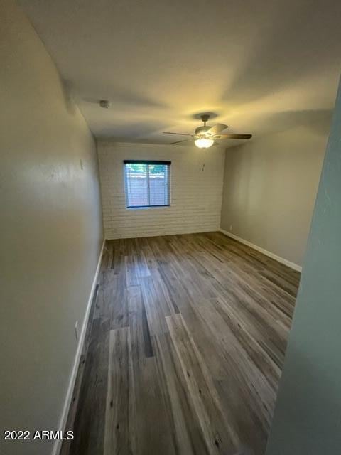 unfurnished room featuring ceiling fan, brick wall, and dark hardwood / wood-style flooring