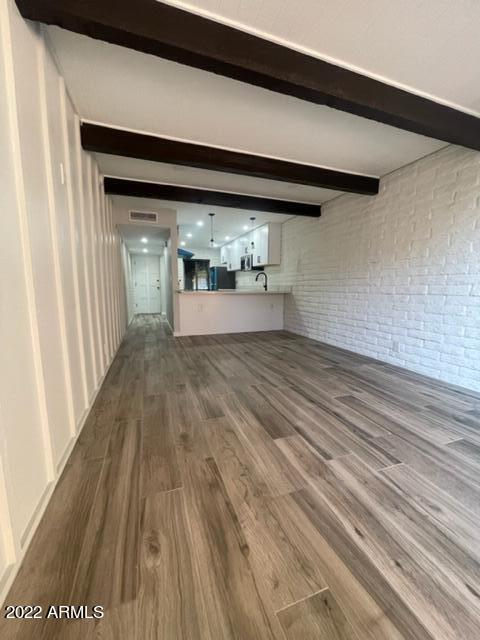 unfurnished living room with dark hardwood / wood-style flooring, beam ceiling, and brick wall