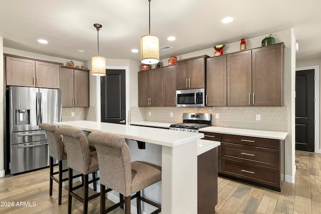 kitchen featuring a center island with sink, hanging light fixtures, dark brown cabinets, and appliances with stainless steel finishes