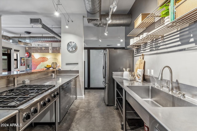 kitchen with stainless steel refrigerator, stovetop, stainless steel counters, sink, and decorative light fixtures