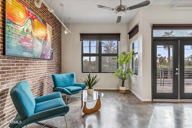 living area with ceiling fan, concrete flooring, french doors, and brick wall