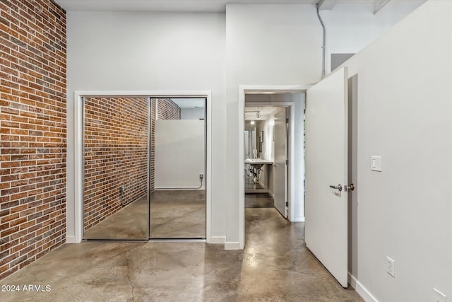 unfurnished bedroom with a high ceiling, brick wall, concrete floors, and a closet