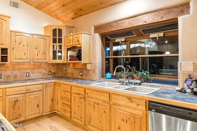 kitchen with backsplash, light hardwood / wood-style flooring, stainless steel dishwasher, vaulted ceiling, and tile counters