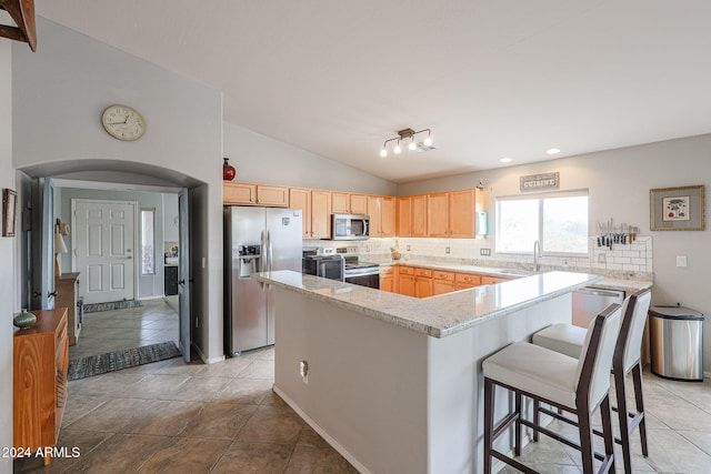 kitchen with light stone countertops, stainless steel appliances, lofted ceiling, decorative backsplash, and light brown cabinetry