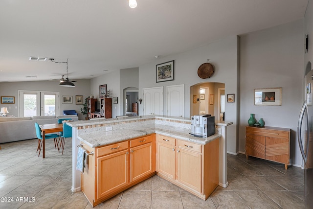 kitchen featuring ceiling fan, a center island, light stone counters, and vaulted ceiling