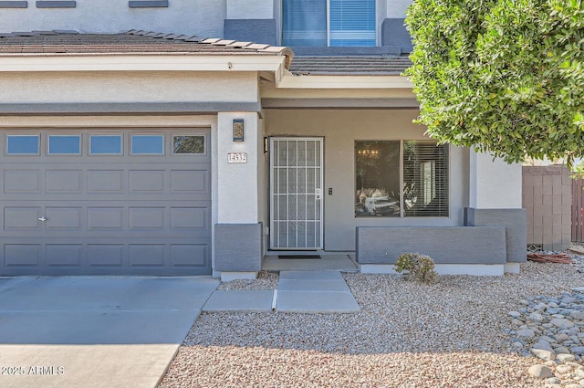 doorway to property featuring an attached garage, concrete driveway, and stucco siding