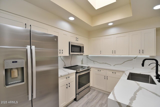 kitchen featuring sink, light stone counters, stainless steel appliances, decorative backsplash, and white cabinets