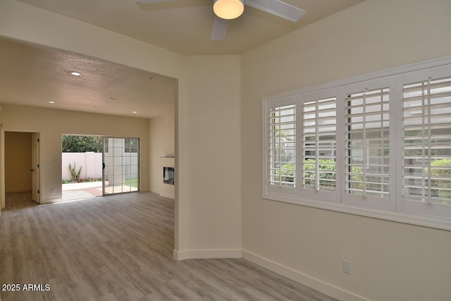 spare room with ceiling fan, a fireplace, a textured ceiling, and light wood-type flooring