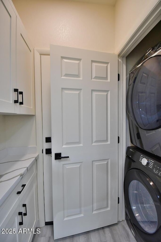 laundry room with cabinets, stacked washer and clothes dryer, and light hardwood / wood-style floors